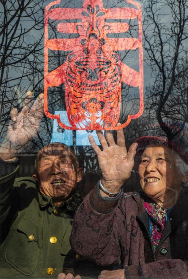 臘月里，霍州市師莊鄉(xiāng)馮南垣村村民師榮光(左)在災(zāi)后重建的新家里貼窗花。(霍州市委宣傳部供圖)