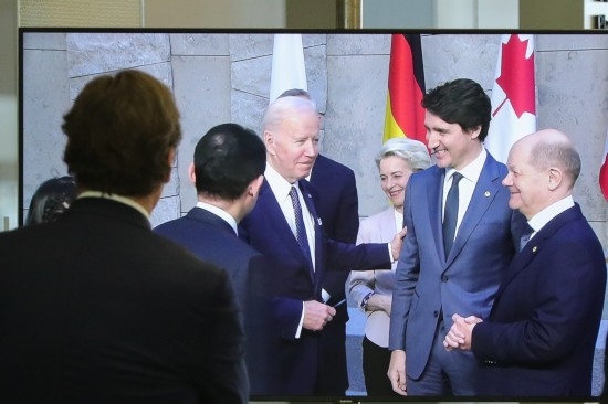 2022年3月24日，在比利時(shí)布魯塞爾的北約總部，一名男子觀看屏幕上美國(guó)總統(tǒng)拜登（右四）、歐盟委員會(huì)主席馮德萊恩（右三）、加拿大總理特魯多（右二）、德國(guó)總理朔爾茨（右一）出席七國(guó)集團(tuán)峰會(huì)合影儀式的畫(huà)面。新華社記者鄭煥松攝