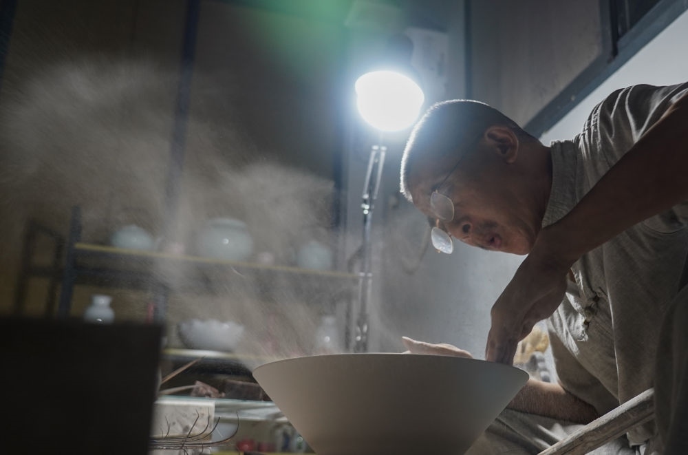 ↑ 在景德鎮(zhèn)，手工匠人吹去坯內(nèi)的泥土（2021年7月14日攝）。