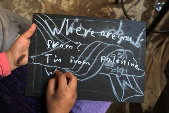 2023年12月28日，一名學生在加沙地帶南部城市拉法一所學校的臨時教室中寫下“我來自巴勒斯坦”的字樣。新華社發(fā)（里澤克·阿卜杜勒賈瓦德攝）