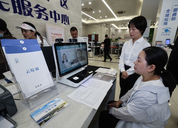 在浙江省嘉興市秀洲區(qū)王江涇鎮(zhèn)便民服務(wù)中心的“跨域通辦·云綜窗”窗口，辦理開業(yè)登記的個體工商戶（右一）通過該系統(tǒng)與江蘇省蘇州市吳江區(qū)盛澤鎮(zhèn)行政審批局工作人員視頻連線，進(jìn)行身份讀取及材料線上審核（2024年5月9日攝）。新華社記者 徐昱 攝