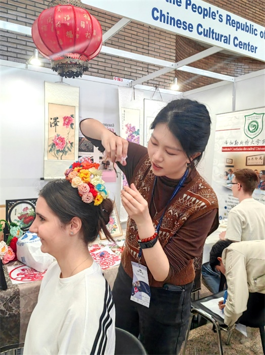 展覽正值羅馬尼亞迎春花節(jié)，國(guó)際中文教師志愿者潘婧穎向游客們介紹了國(guó)家非物質(zhì)文化遺產(chǎn)——福建泉州的簪花文化。布加勒斯特大學(xué)孔子學(xué)院供圖。